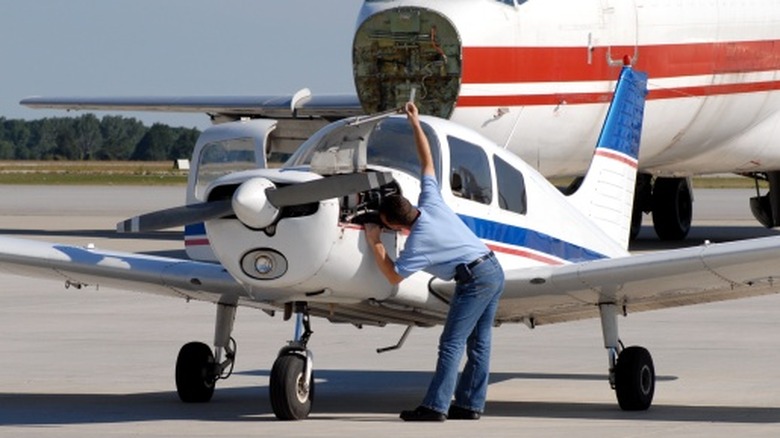 A pilot examining the engine compartment of a small plane