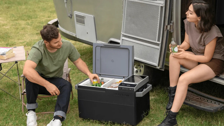 A man and a women using an EcoFlow Glacier cooler box while camped next to an RV.