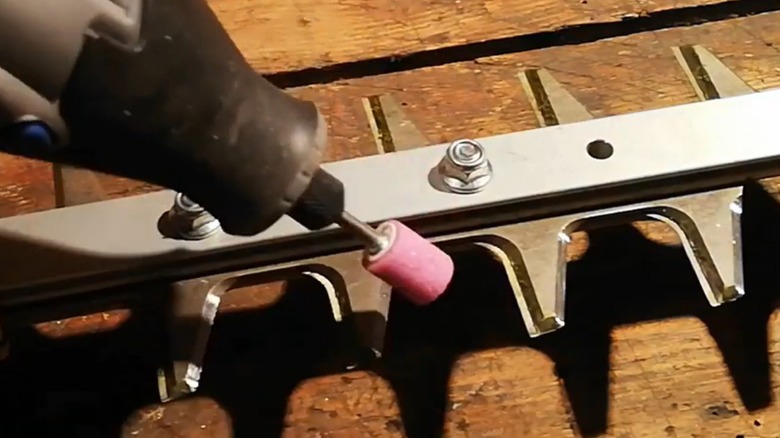 A person using a rotary tool on a hedge trimmer blade.