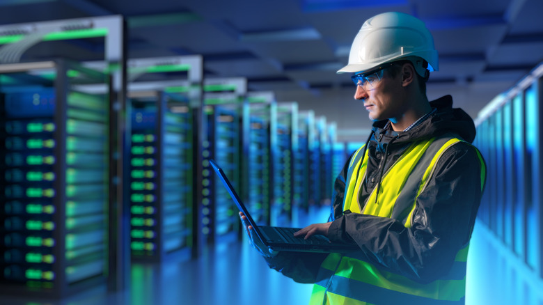 Engineer wearing a hi-vis jacket and hard hat inside a data center full of server racks.