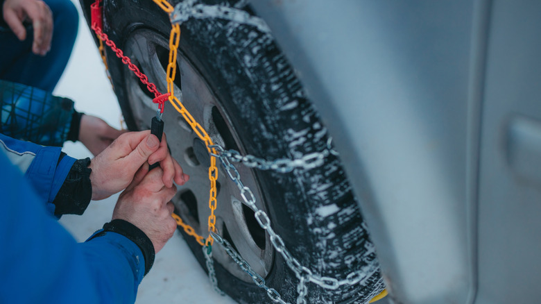 A person installing a colorful set of tire chains on a vehicle.
