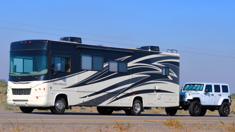 A large Class A motorhome towing a Jeep Wrangler behind it.