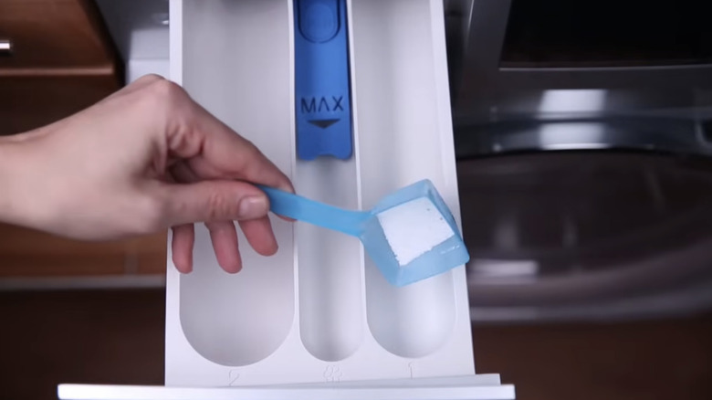 A hand pours washing powder into a machine compartment