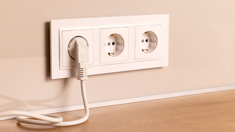 Group of white european electrical outlets with plug inserted into it on modern beige wall