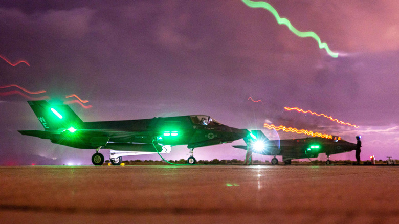 Two fighter planes on the ground with green lights showing on both.