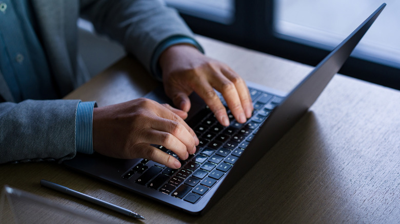 Business professional using laptop computer with both hands on keyboard