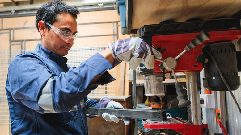 A worker drilling metal in workshop using bench drill press
