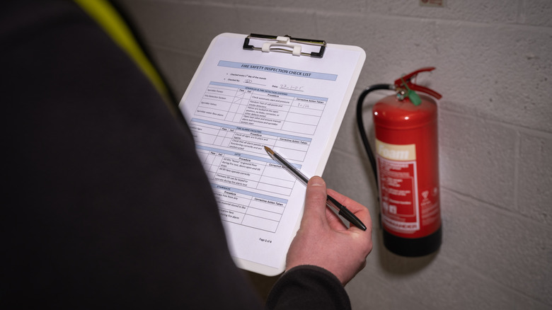 Safety inspector checking out fire extinguisher and writing on a check list