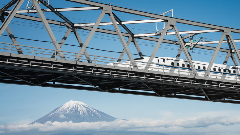 Shinkansen train passes over bridge with snowy mountain in background