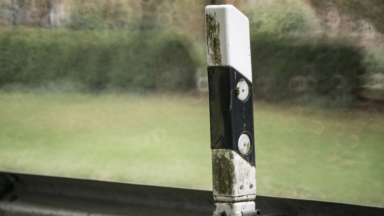 A highway reflector post attached to a guardrail covered in green dirt