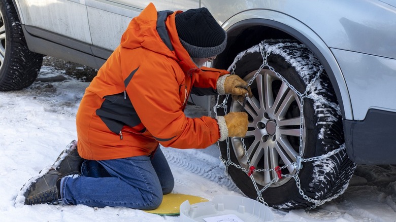 driver installing tire chains in snow