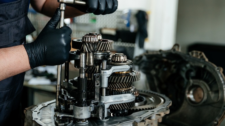 Mechanic servicing manual transmission, showing complete gearbox assembly