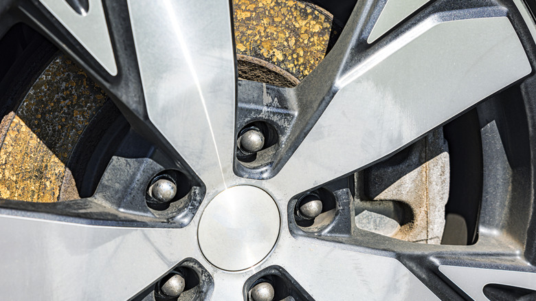 A rusty brake rotor behind a wheel.