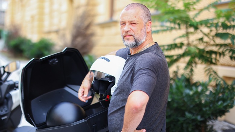 A man stowing motorcycle helmets in a trunk on the back of a motorcycle.