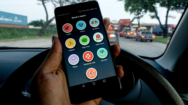 person holding a smartphone showing the send a report screen on Waze inside a car