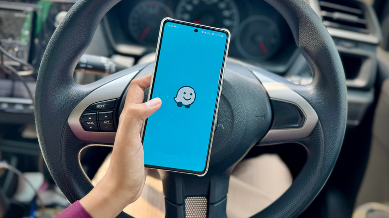 person holding a smartphone running the Waze app in front of the steering wheel inside a car