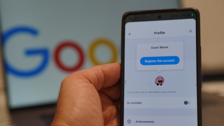 person holding a smartphone showing the Waze profile screen in front of a laptop