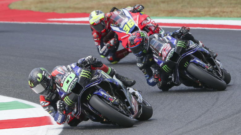 Three sports motorcyle riders cornering at a steep angle on a racetrack.