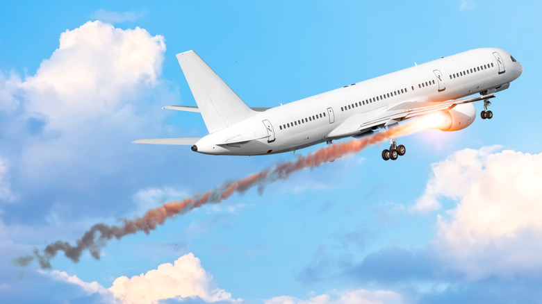An airplane with a burning engine leaves a smoke trail.