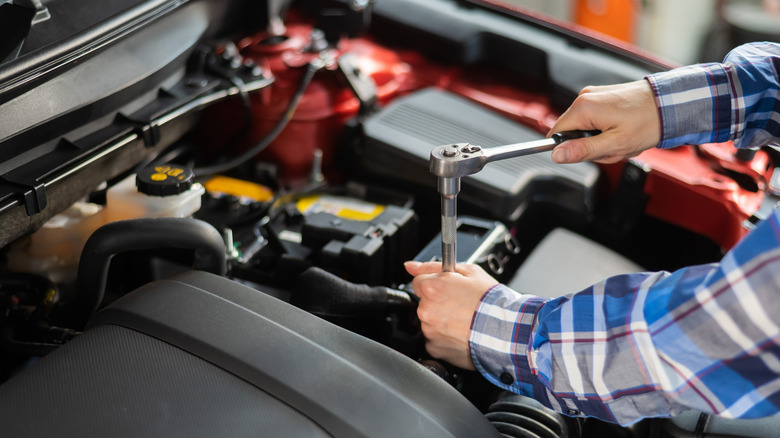 Mechanic servicing spark plug with hand ratchet