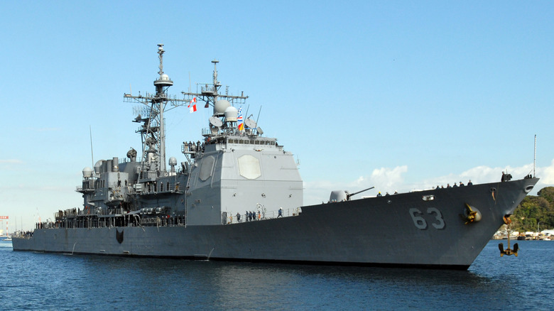 Close up starboard side angled view of the Ticonderoga-class cruiser USS Cowpens underway on the water against clear skies.