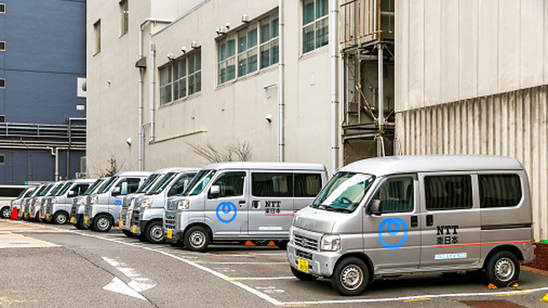 Line of NTT Tokyo 3-cylinder equipped kei trucks parked in lot, left-side view