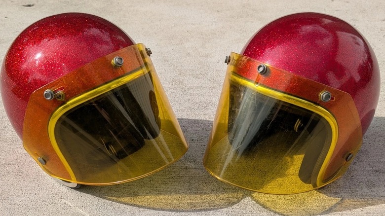 Two 1970s motorcycle helmets on concrete.