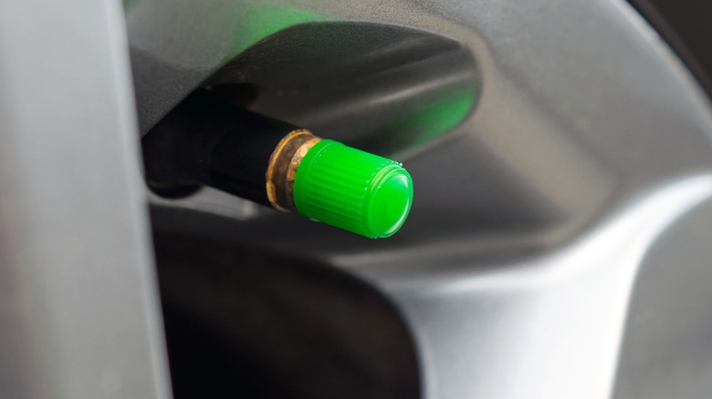a closeup image of a car's wheel and tire with a green valve stem cap
