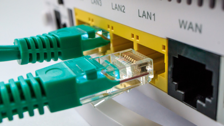 The back of the router showing the ethernet ports. One green ethernet cable is slotted into a port. The other is the in the process of being slotted in.