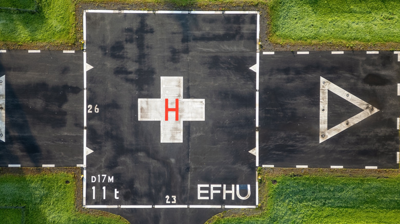 Top-down view of a hospital helipad with a white cross and red "H"