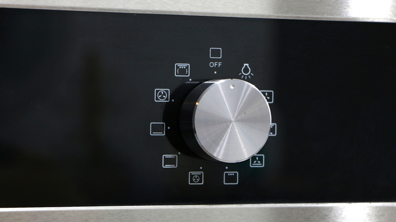 A close-up of a silvery oven knob with square symbols around it