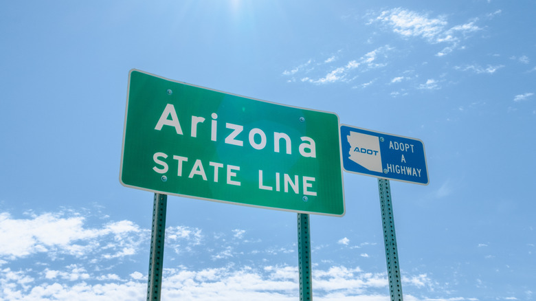 Arizona state line sign with an adopt a highway sign next to it