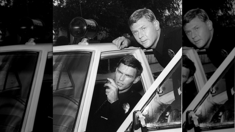 Actor Martin Milner leans over the door of a patrol car as Kent McCord talks on the police radio in a promotional still for the television series, 'Adam 12,' c. 1969.