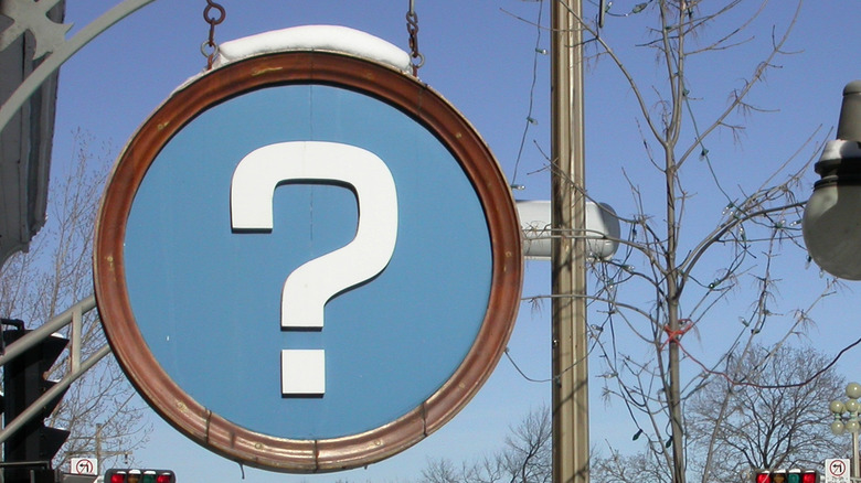 Blue road sign with question mark on it mounted on a telephone pole.