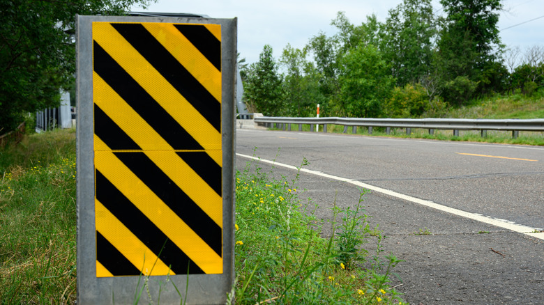 View of black and yellow diagonal striped road sign in front of a bridge.
