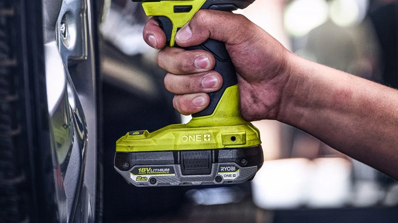 Hand holding a power tool with a Ryobi battery on the bottom
