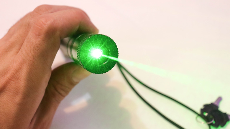 A hand holding a high-powered green laser pointer while on