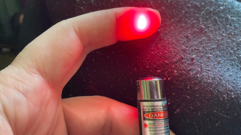 A handheld laser pointer shines onto a person's finger