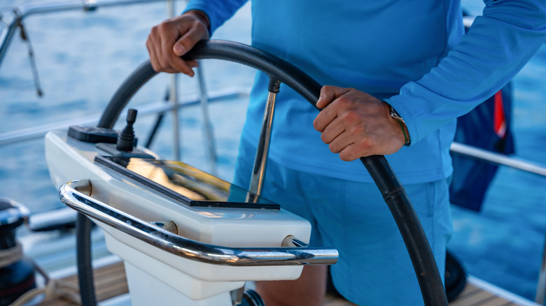 Man's hands on steering wheel of boat.
