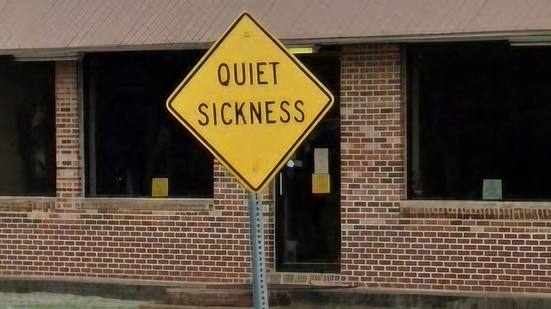 A tall, yellow Quiet Sickness sign