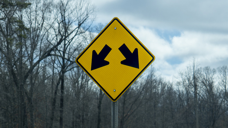 Yellow diamond warning road sign with two arrows pointing down on a forest road