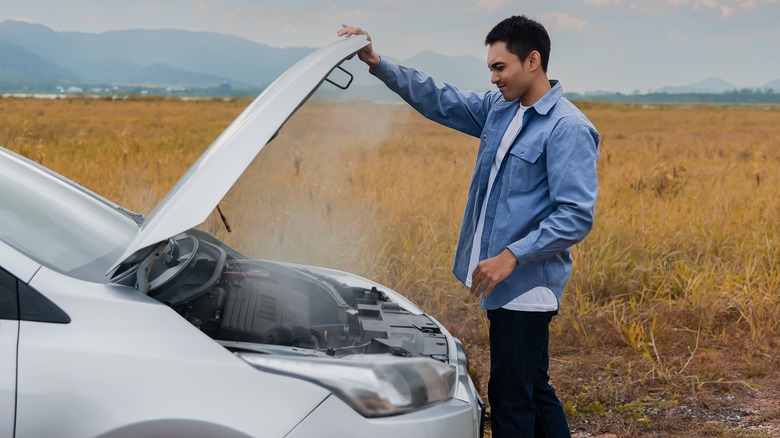 Person looking under hood of overheated car