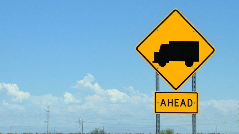 yellow-colored road sign with a black truck on it on the roadside