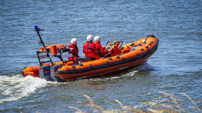 An orange rescue boat shown moving through the water with three rescuers