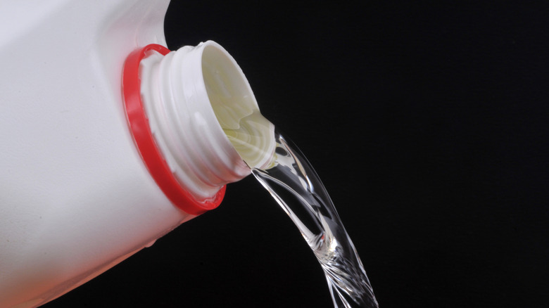 A close-up of bleach pouring from a canister on a black background