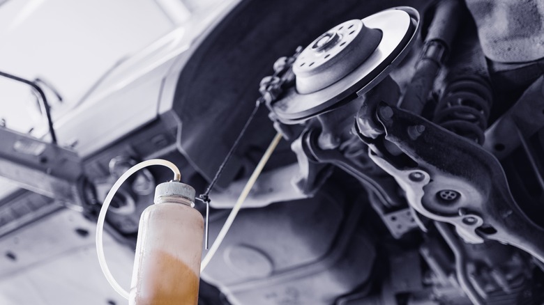 An off-screen mechanic flushing out the brake fluid from a car's brakes