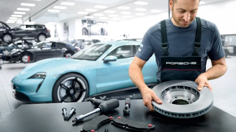 Brake service being carried out by a technician, blue Porsche Taycan in the background