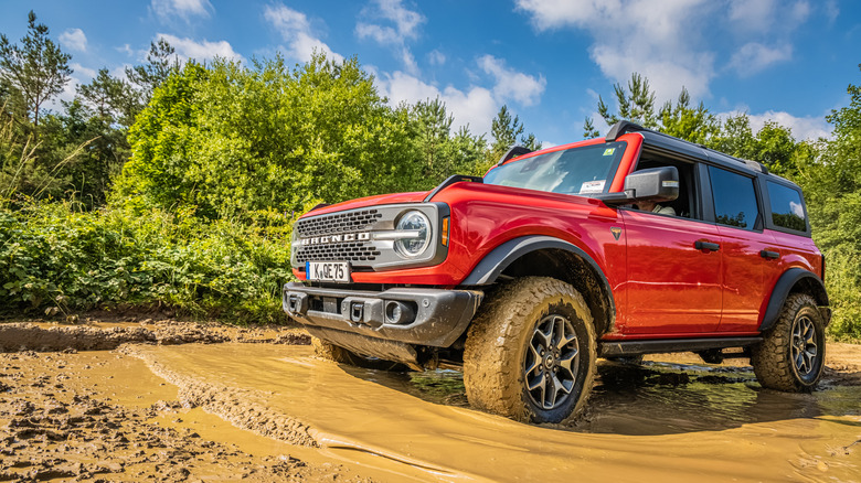A red Ford Bronco driving through a very muddy puddle.