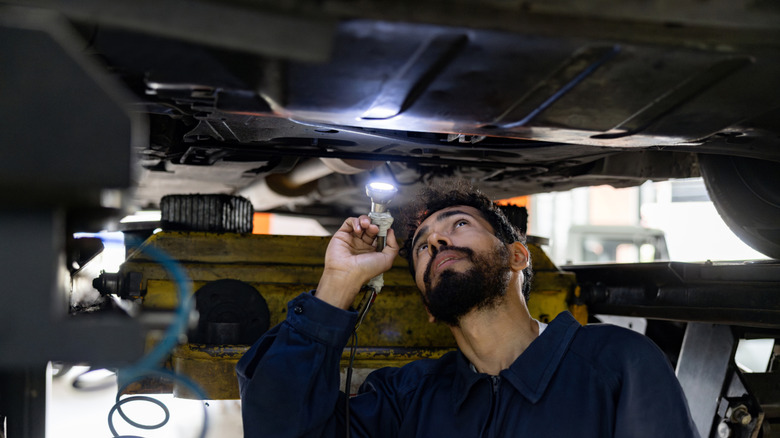 A person using a flashlight to investigate the underside of a vehicle
