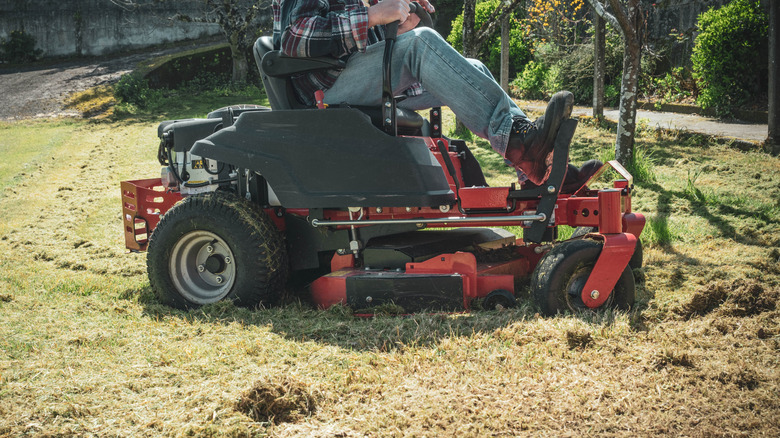 A person cutting thick grass on a riding mower.